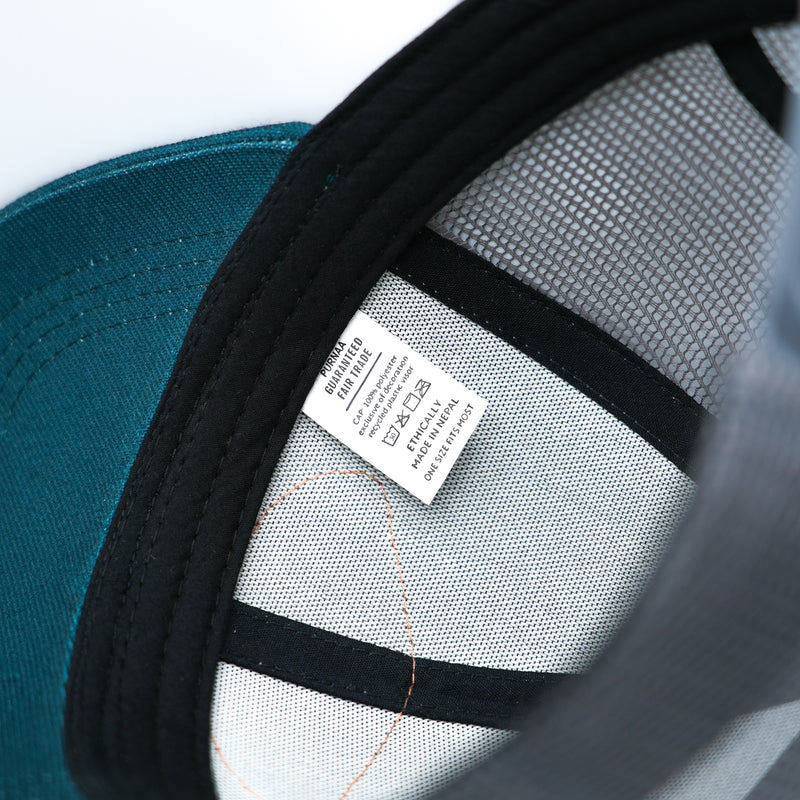 This image shows the interior of the Fair Flies teal LoPro Trucker cap hat with the Purnaa Guaranteed Fair Trade tag.  One size fits most.  Made in Nepal.